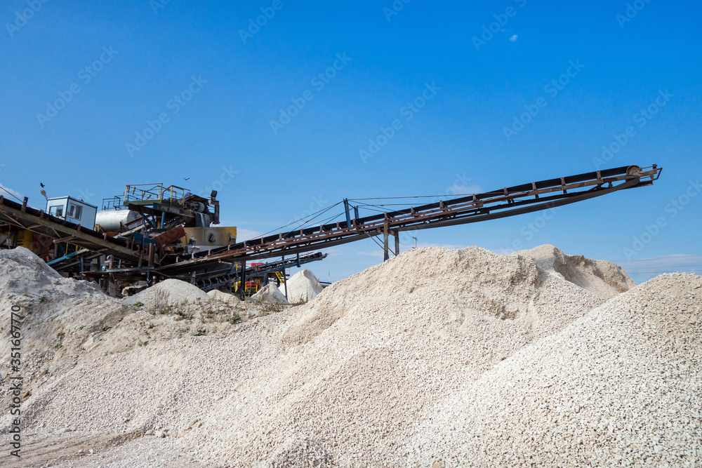 Conveyor of stone-crushing plant & stockpiles of quarry products: limestone after preparing. Rocks are ready to be loaded in trucks