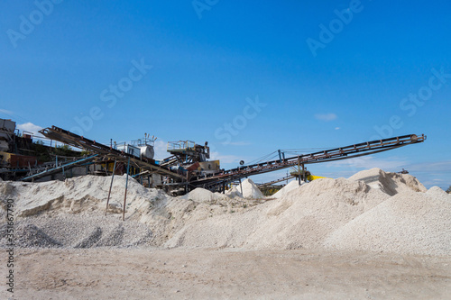 Stone-crushing plant & its conveyor. Stockpiles of quarry products are on front of picture.  Limestone rocks are ready to be loaded in trucks after preparing