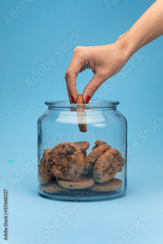 A woman hand taking cookies from a glass jar on blue background. photo