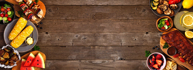 Summer BBQ or picnic food double side border over a rustic wood banner background. Various grilled meats, vegetables, fruits, salad and potatoes. Above view with copy space.