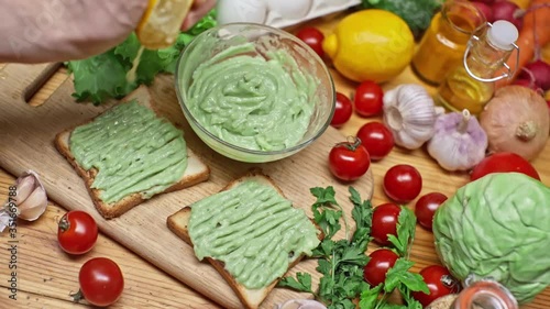 Closeup Of Hand Squeezes Lemon On Toast With Avocado. View of a table with a variety of fresh food on the table. Cooking a delicious healthy vegetarian breakfast  in slow motion. Healthy eating.