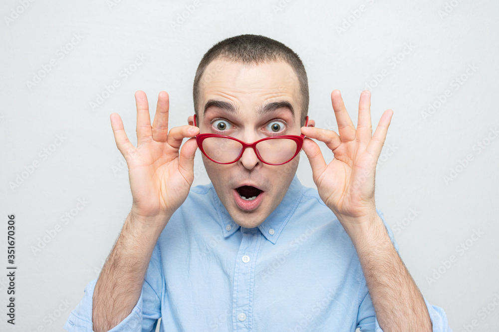 Stunned nerd guy in red glasses looks at the camera, portrait, white background Stunned nerd guy in red glasses looks at the camera, portrait, white background