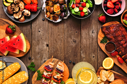 Summer BBQ or picnic food frame over a rustic wood background. Assortment of grilled meats, vegetables, fruits, salad and potatoes. Top down view with copy space.
