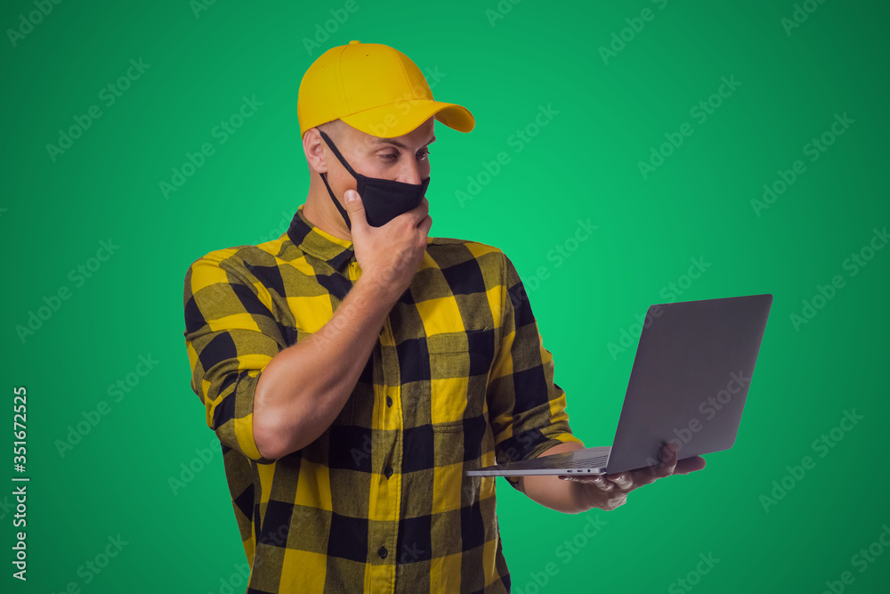 young man in mask with laptop on green background