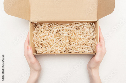 Woman shows an open gift box with decorative straw or shavings, women's hands, closeup, copy space, top view