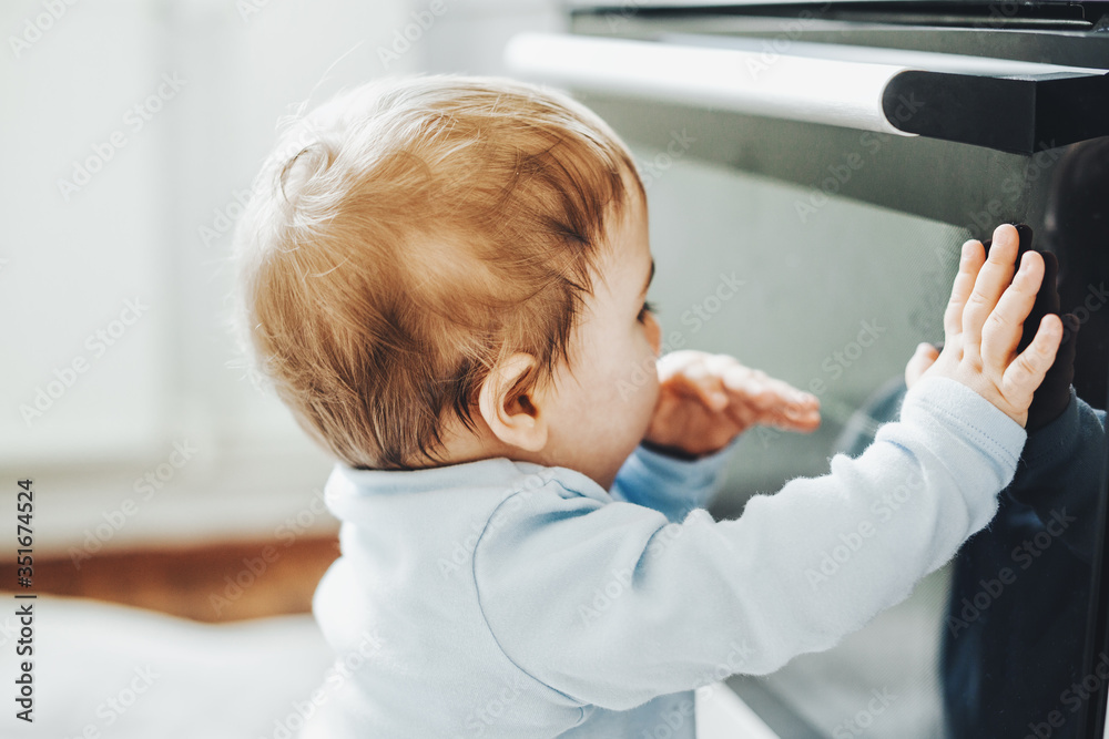 Baby boy touching oven door in the kitchen Baby boy touching oven door in the kitchen