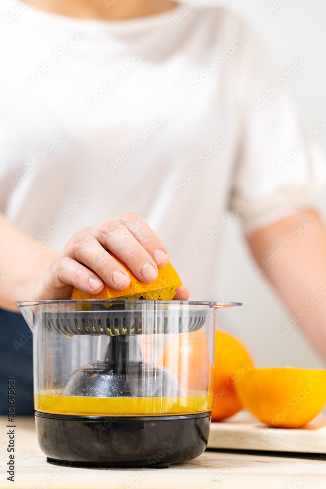 a woman's hand squeezing half an orange in a juicer a woman's hand squeezing half an orange in a juicer