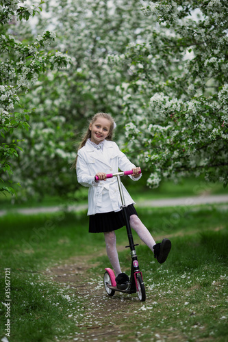 Cute little girl riding a scooter Child on scooter in park. Outdoor activity for children on safe blooming park.