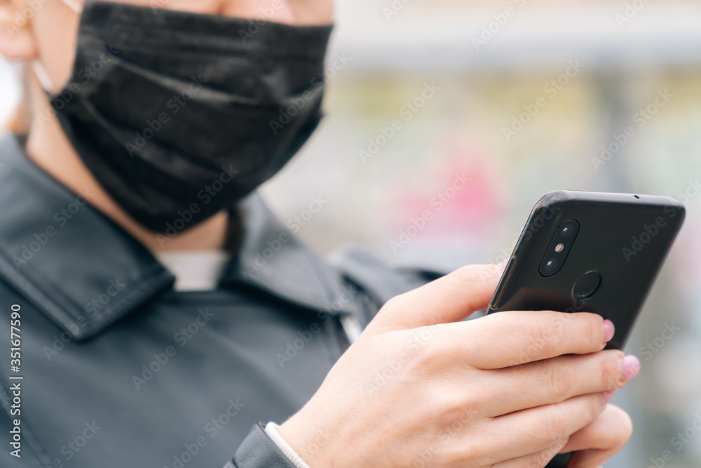 Close-up women's hands hold a phone against the background of a face in a medical mask. The concept of safety is about your health. Girl calls taxi Close-up women's hands hold a phone against the background of a face in a medical mask. The concept of safety is about your health. Girl calls taxi