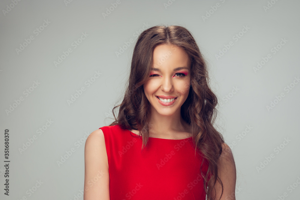 Beautiful young woman with long healthy curly hair and bright make up wearing red dress isolated on grey studio backgroud. Beauty and fashion, hair and skin care, treatment concept. Well-kept girl. Beautiful young woman with long healthy curly hair and bright make up wearing red dress isolated on grey studio backgroud. Beauty and fashion, hair and skin care, treatment concept. Well-kept girl.