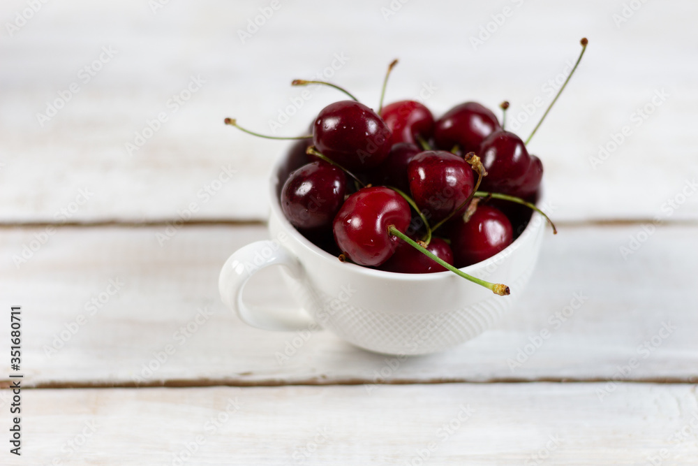 Cup with ripe red cherries on a white wooden rustic background Cup with ripe red cherries on a white wooden rustic background