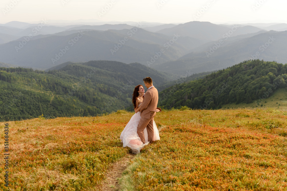 The bride and groom are hugging. Sunset. Wedding photo on a background of autumn mountains. A strong wind inflates hair and dress. Close-up.