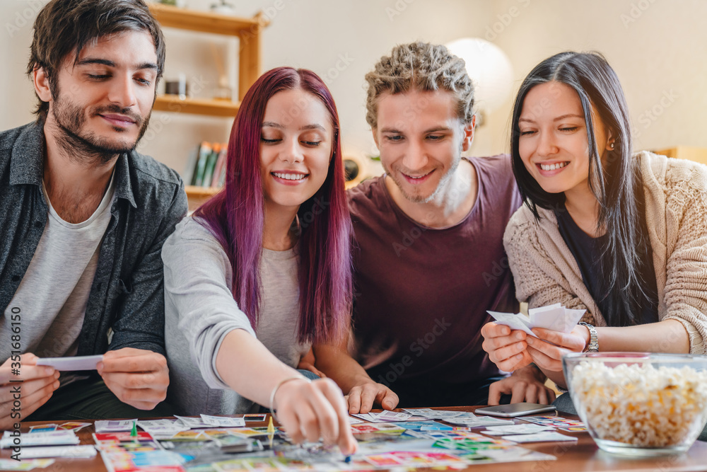 Fototapeta premium Young group of friends playing board game on table at home interior