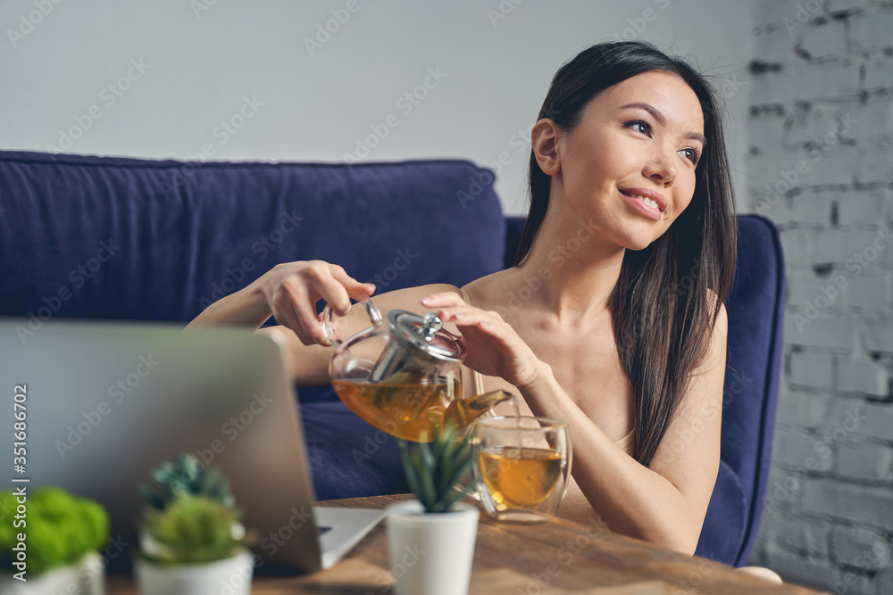 Joyful young woman drinking tea and using laptop Joyful young woman drinking tea and using laptop
