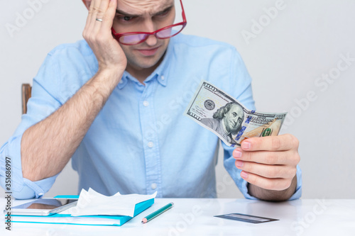 Wallpaper Mural Guy with dollars is upset about finances, calculates the family budget, bills on the desktop Torontodigital.ca