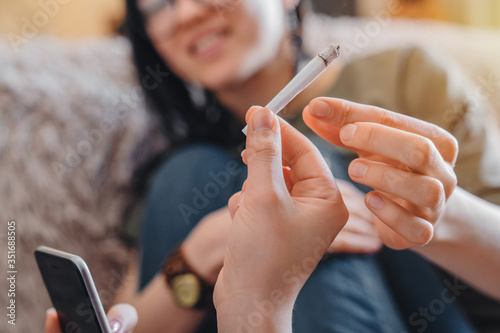 Close up of young caucasian women smoking weed at home. Focus on joint