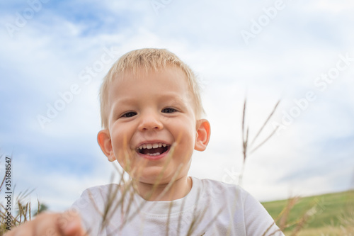 Happy little blond boy outdoors smiling on grass field