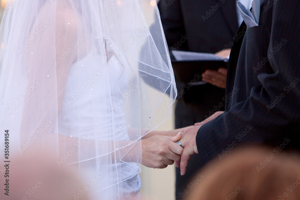 Bride and groom holding hands, facing each other with pastor in officiant in background