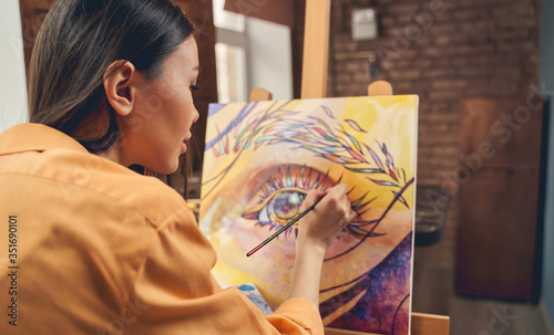 Fototapeta Naklejka Na Ścianę i Meble -  Beautiful young woman painting eye on easel at home