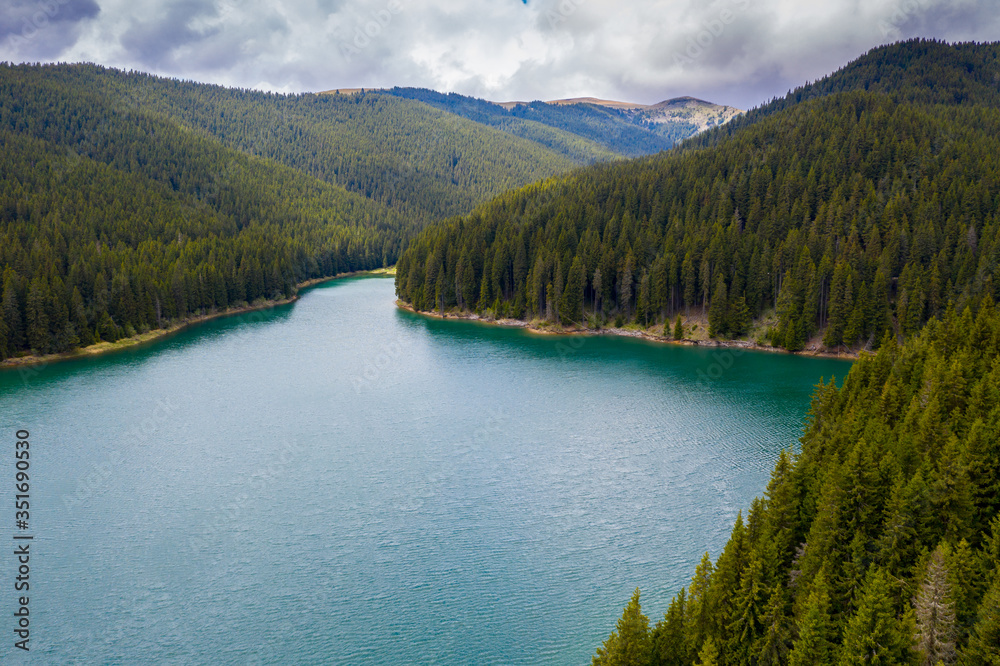 Turquoise water in a mountain forest lake with pine trees. Aerial view of blue lake and green forests. View on the lake between mountain forest. Over crystal clear mountain lake water. Fresh water