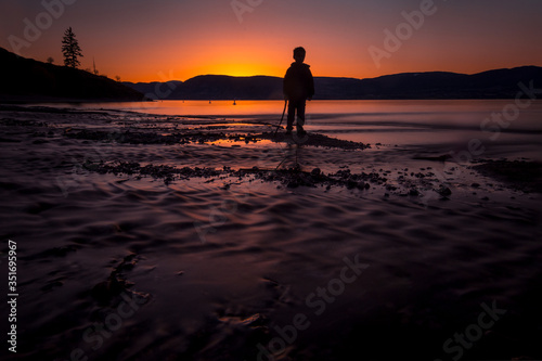 Silhouetted Boy During Sunset By The Shore With Flowing Water
