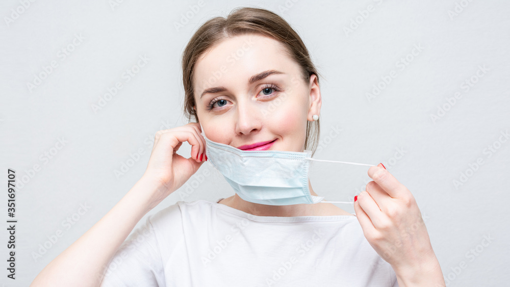 Woman taking off her medical mask, portrait, close up, white background, 16:9 Woman taking off her medical mask, portrait, close up, white background, 16:9