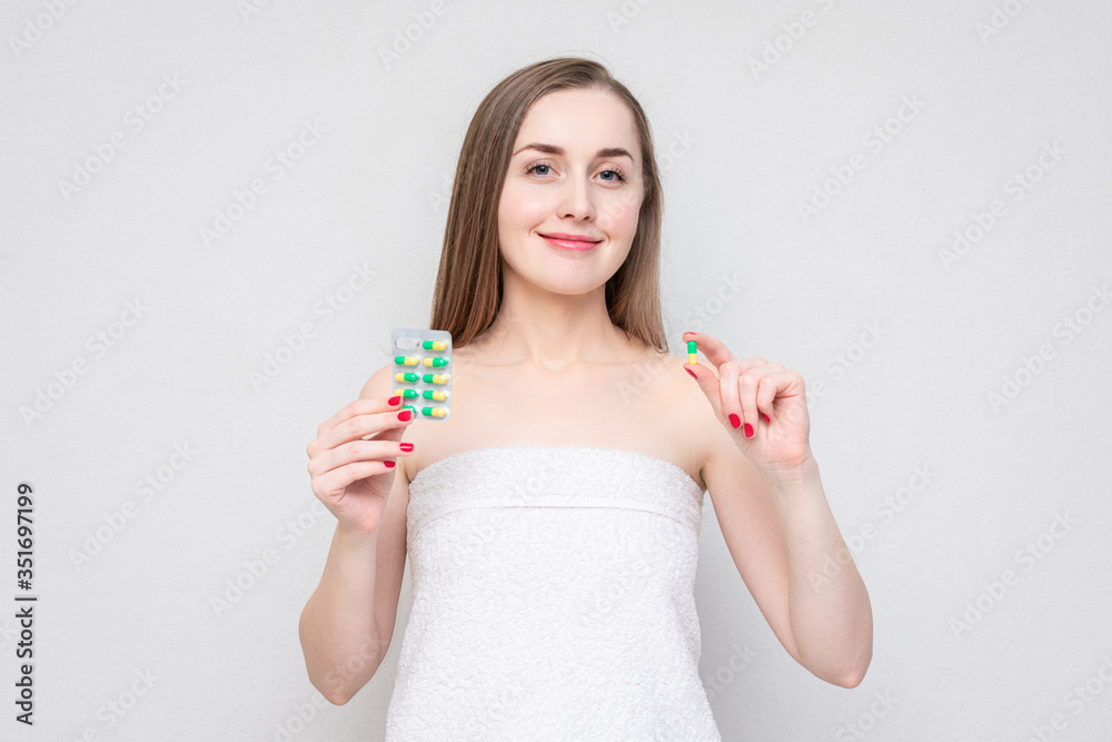 Girl in towel shows green pills, white background Girl in towel shows green pills, white background