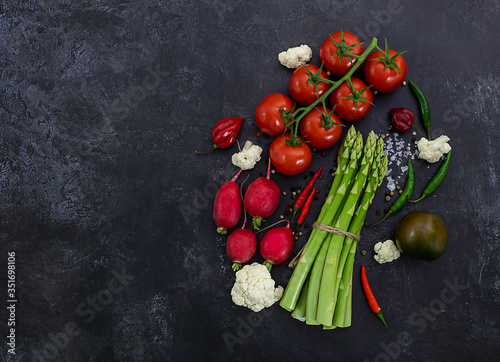 Fresh raw vegetables on black background. Tomatoes, peppers, green asparagus, radish, cauliflower. Flat lay, top view, copy space