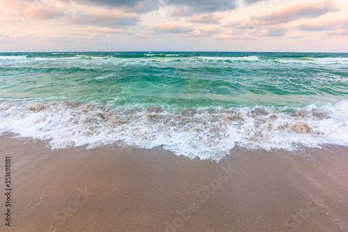 golden beach and green sea on a cloudy evening. beautiful view of waves rolling the coast beneath a glowing sky