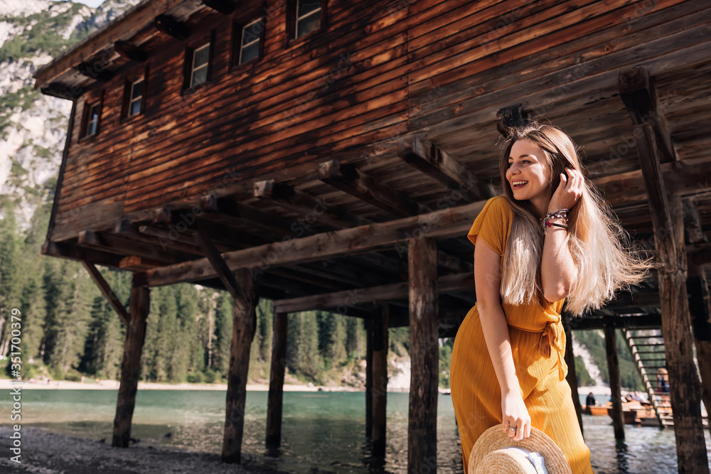 girl with long hair posing near a wooden building by the mountai
