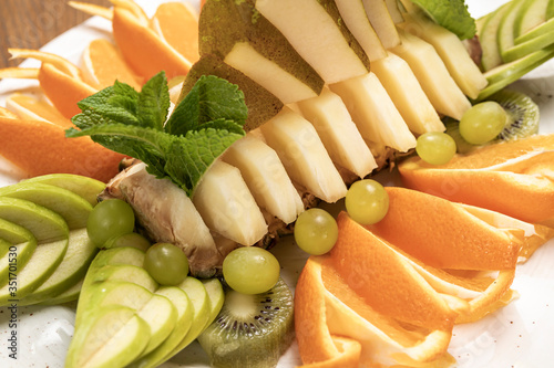 tropical fruit sliced with green grapes, kiwi, pineapple, oranges, apples assorted on a white plate