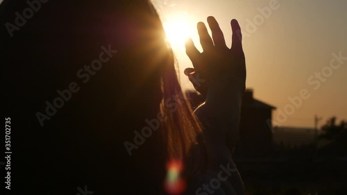 close-up of a woman's hand in silhouette touching the sun rays in a field