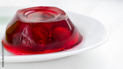 White plate with cherry berries in red jelly on a white background.