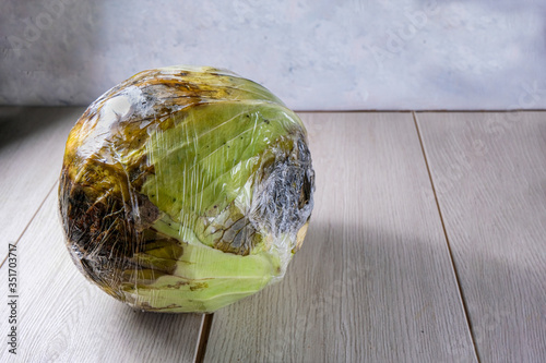 The cabbage is wrapped in cellophane. A spoiled vegetable. The concept of Ugly products, no plastic packaging. Copy space