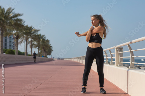 Portrait of a young woman stretching hands isolated. Portrait of a fitness woman doing warm up exercises outdoors. Attractive woman stretching. Young fit woman athlete stretching before run. Dubai 