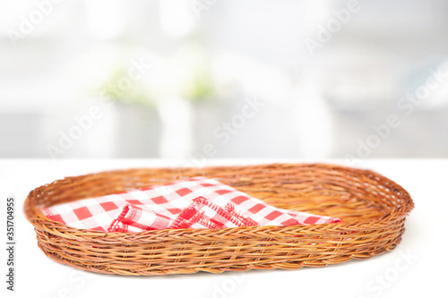 
Oval-shaped wicker basket and checkered cotton napkin inside on a white table table photo