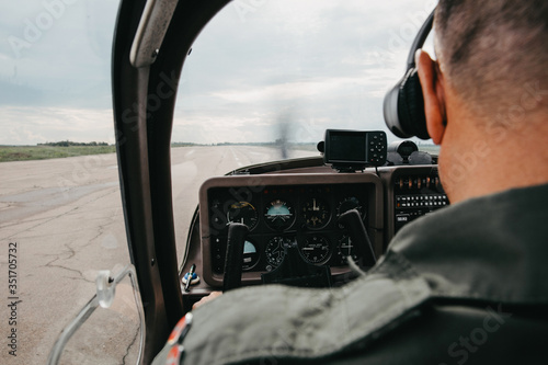 Pilot in cockpit. Aircraft Pilot at work. Rear view of pilots. Rear view of commercial pilot wearing headset and uniform sitting inside aircraft cockpit in front of dashboard with numerous buttons. 