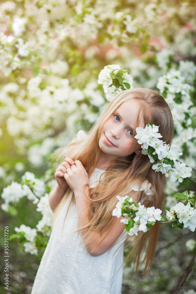 Fototapeta premium Beautiful preteen girl with long blond hair enjoy spring apple blooming. Little preschool girl in garden tree flowers. Vertical shot with copy space.