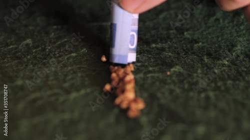 A tube from a banknote sucks buckwheat on a green cloth. Close-up.