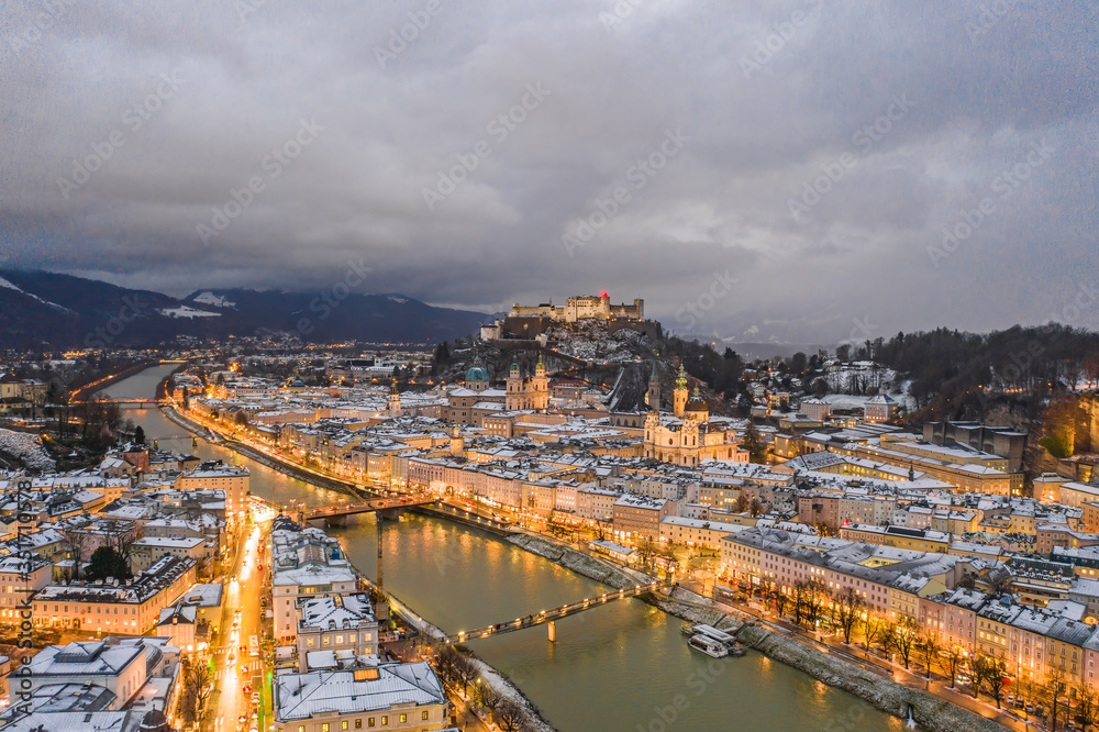 Aerial drone view of Salzburg snowy old town with city light on at dusk hour in winter