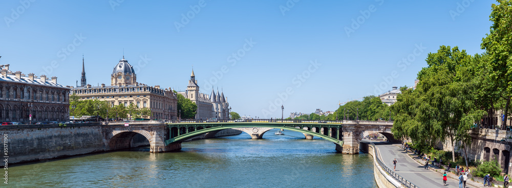 Fototapeta premium Panoramic view of the Tribunal de Commerce, the Conciergerie, Pont Notre Dame and Parisians walking on the embankment - Paris, France