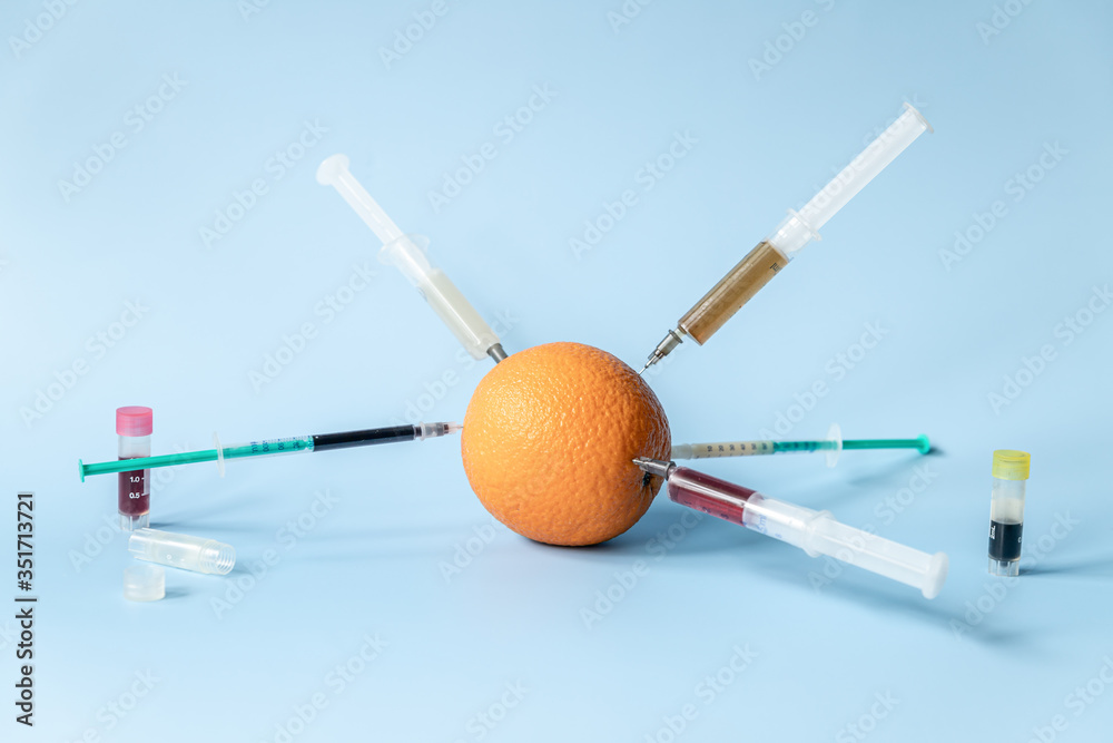 Orange with stuck syringes with liquid on a blue background. Modified concept of unhealthy fruits Orange with stuck syringes with liquid on a blue background. Modified concept of unhealthy fruits