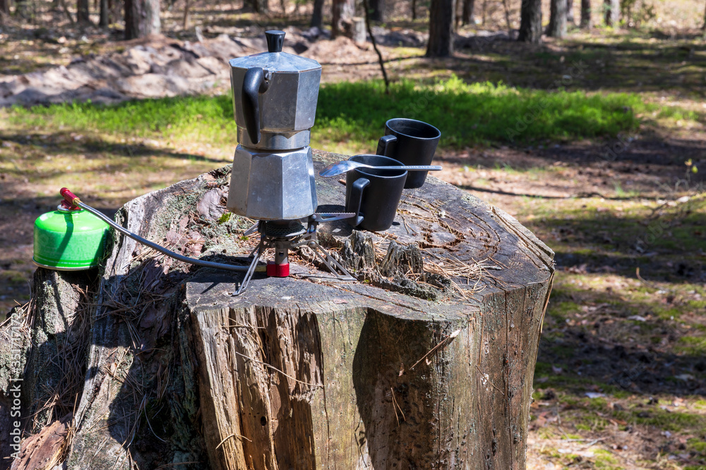 Moka pot coffee maker and two coffee cups on cut stump. Using small tourist gas stove in forest place. Poland, Europe. Moka pot coffee maker and two coffee cups on cut stump. Using small tourist gas stove in forest place. Poland, Europe.