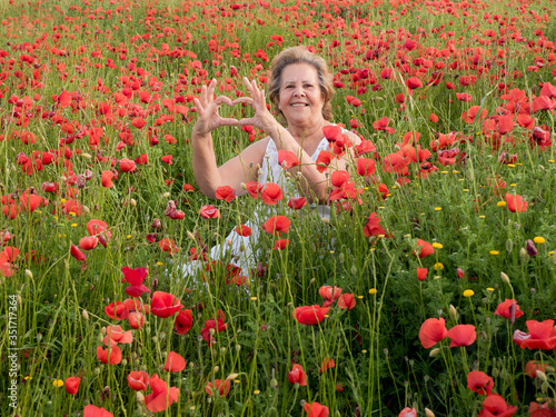 Freedom and happiness in an elderly lady who draws a heart among poppies in spring