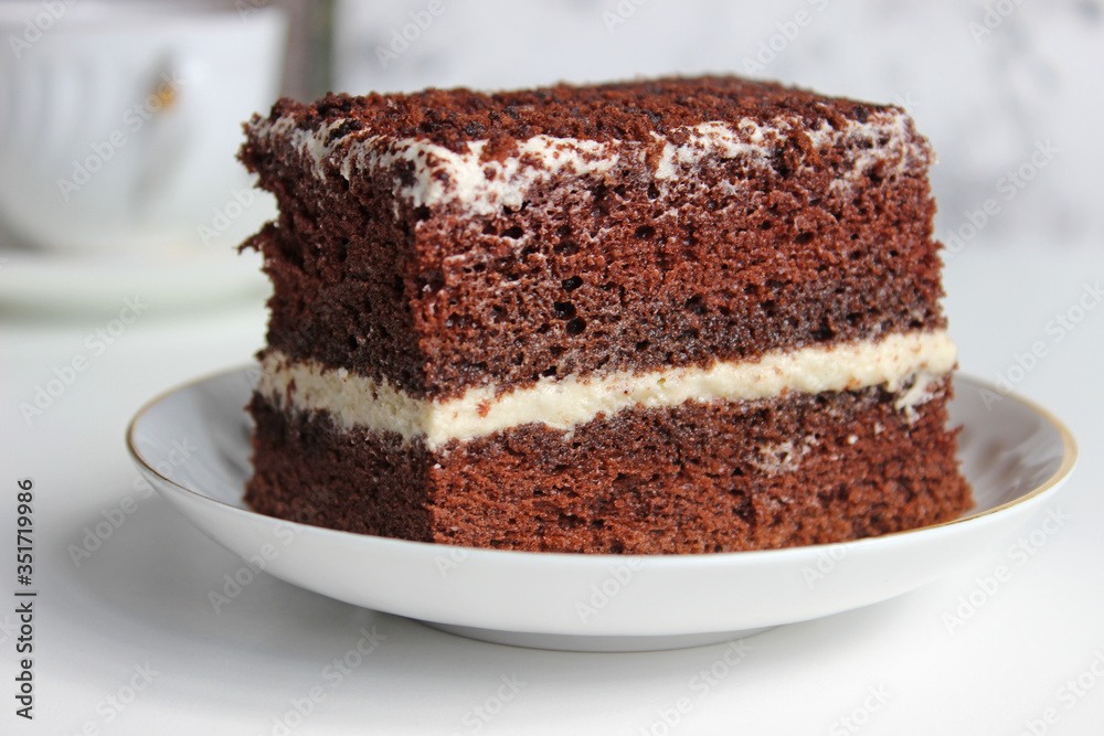 A slice of chocolate cake with white cream with a curl on a light background. A slice of chocolate cake with white cream with a curl on a light background.