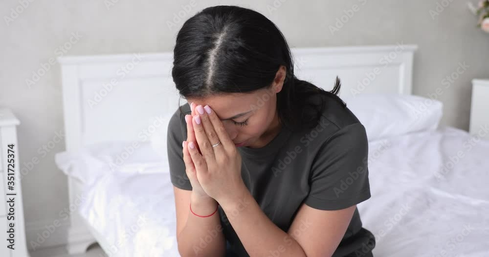 Hopeful young african american woman sitting on bed with folded hands, saying morning worship. Faithful 30s mixed race lady praying God, asking for help or waiting for miracle alone in bedroom. Hopeful young african american woman sitting on bed with folded hands, saying morning worship. Faithful 30s mixed race lady praying God, asking for help or waiting for miracle alone in bedroom.