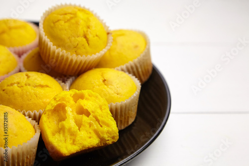 Pumpkin muffins on black plate on white wooden table. Halved cupcake