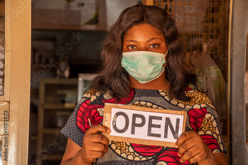 local african business owner holding a open sign in her store