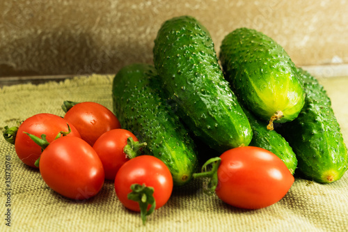 Ripe cherry tomatoes and cucumbers stacked on a tablecloth