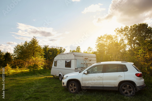 White car and white trailer in nature on a warm day at sunset, calm, motor home, family holiday in the outdoors. Camping car in the wood